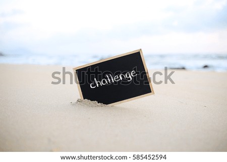 A blackboard half inside sand near beach with word - challenge.