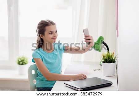 people, children and technology concept - girl with laptop computer and smartphone taking selfie at home
