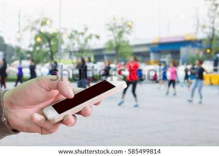 Man use mobile phone, blur image of Aerobic dance in the park as background. 