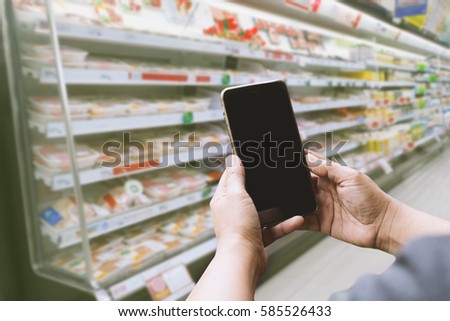 hand of women using smartphone and blank screen with blurred background and green filter of supermarket or grocery for price; online shopping conceptual