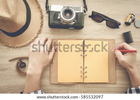 Notebook, film camera, wicker hat and sunglasses on wooden table - top view.