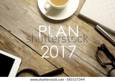 Business concept. Top view of tablet pc, magnifying glass, pen, notebook, glasses and a cup of coffee with PLAN 2017 written on wooden table.