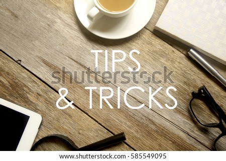 Top view of tablet pc,magnifying glass, notebook, pen, glasses and a cup of coffee with TIPS AND TRICKS written on wooden table.