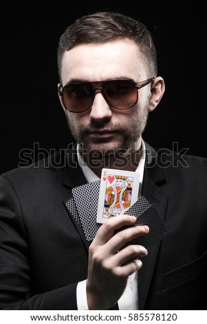 The poker player in black glasses, in a casino with open one card. On a black background.