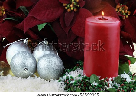 Burning Christmas candle surrounded by rich burgundy colored Poinsettias, silver ornaments and snow.