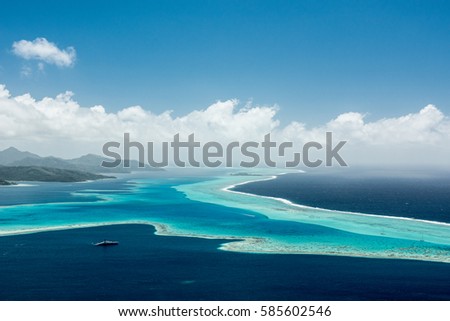 Aerial view on lagoon with blue and turquoise water, barrier reef, blue sky and white clouds of Raiatea island in French Polynesia