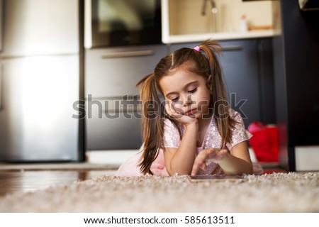 Bored little girl looking at tablet. Loneliness childhood.