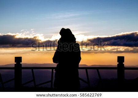silhouette of a beautiful woman standing on panoramic viewpoint., looking to the horizon and enjoying a beautiful sunset behind the mountain.