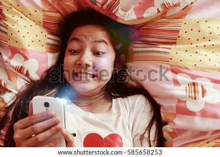 cropped image of teenage girl lying in bed while excitedly playing with her mobile  phone