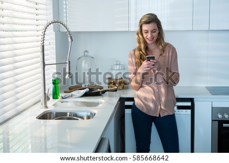 Woman using mobile phone in kitchen at home