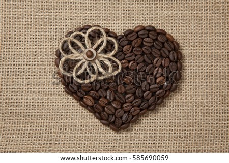 Heart of coffee beans with jute flower on sackcloth.
