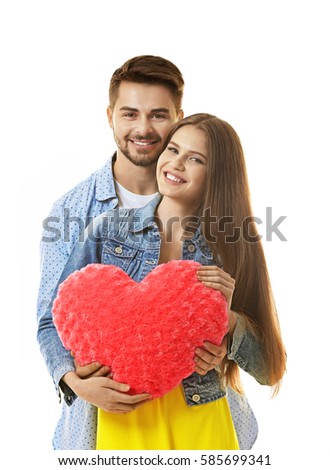Cute young couple with cushion in shape of heart on white background
