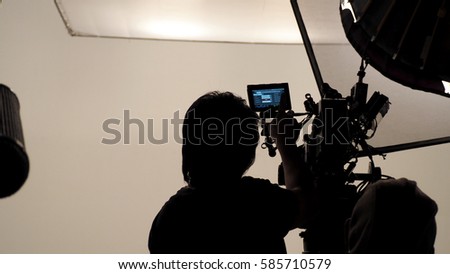 Silhouette of photographer checking for movie camera and set before shooting in studio.