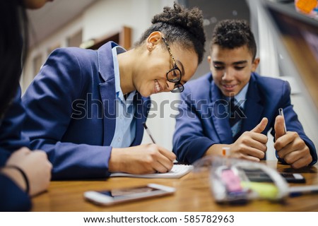 Teen students are working together and taking notes in lesson time at school.  Royalty-Free Stock Photo #585782963