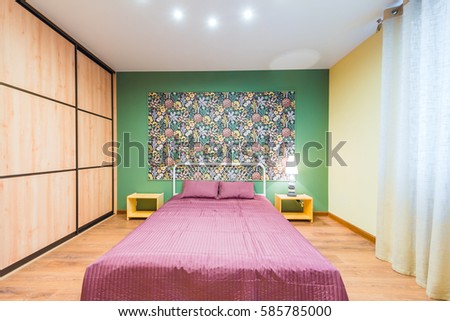 Interior bedroom with a large double bed with bedside tables, picture on the wall on a background of modern wallpaper