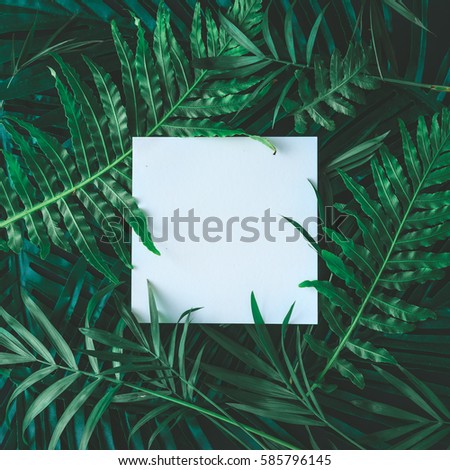 Creative layout made of tropical flowers and leaves with paper card note. Flat lay. Nature concept
