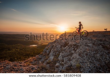 Active life /
A woman with a bike enjoys the view of sunset over an autumn forest