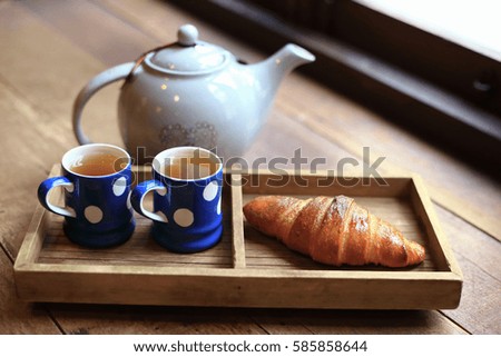 The hot tea in the cups with croissants, as wood background or print card.