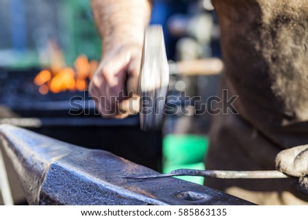 Blacksmith hammering hot iron rod on anvil against the background of fire