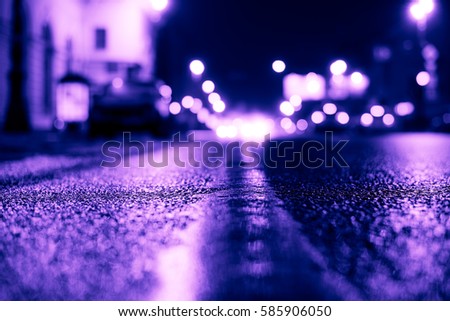 Rainy night in the big city, the headlights of the approaching cars on the road. Close up view from the level of the dividing line, image in the purple-blue toning
