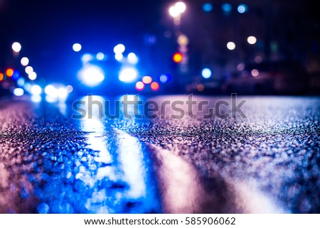 Rainy night in the big city, the arriving car on the road. Close up view from the level of the dividing line, image in the blue tones