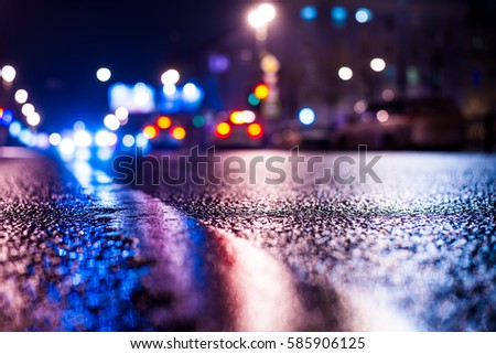 Rainy night in the big city, the passing cars on the road. Close up view from the level of the dividing line, image in the blue tones