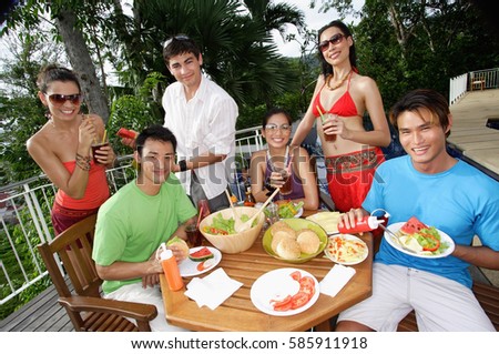 Young adults having a meal on patio, smiling at camera