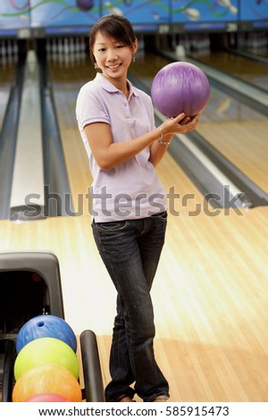 Woman at bowling alley holding bowling ball, smiling