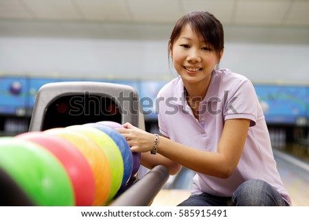 Woman selecting ball at bowling alley, smiling at camera