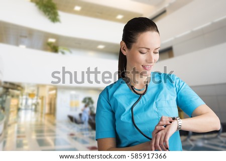 beautiful woman doctor or nurse standing in a hospital lobby looking at her watch