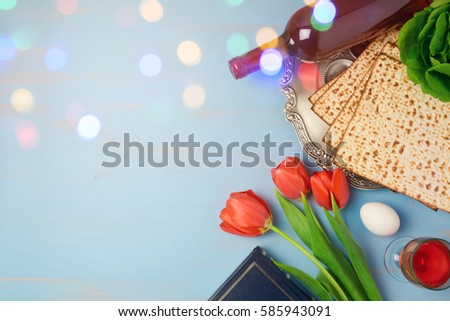 Passover holiday concept seder plate, matzoh and tulip flowers on wooden background with bokeh overlay. Top view from above