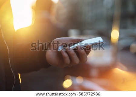 The man holding modern smartphone outdoor, Close-up of male hand using the phone with sunset on the background, sunset light, golden light, soft focus