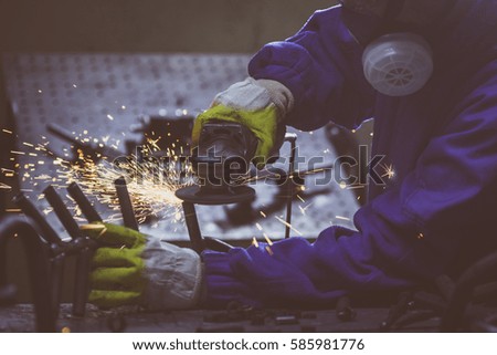 Craftsman grinding steel pipe with an electric disk grinder in the workshop.