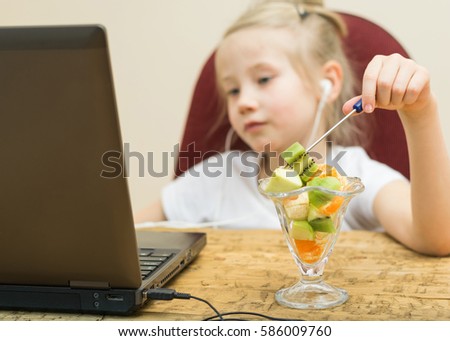 Girl eating fruit salad at the laptop. Healthy Eating child at the computer.