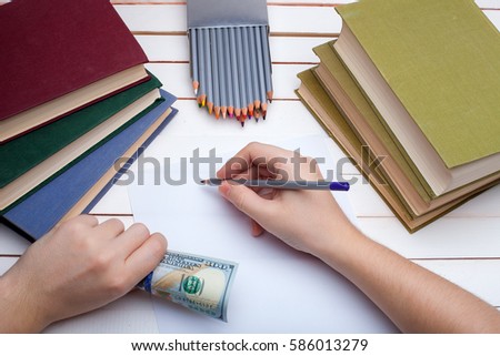 On a wooden table hardcover books with a pencil and the sheet of paper on which in hands the pencil draw.