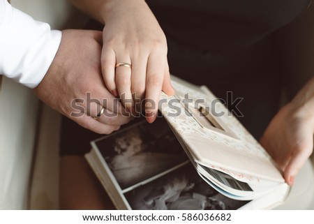 Man and woman watching a photo album beige close-up of hands in wedding rings