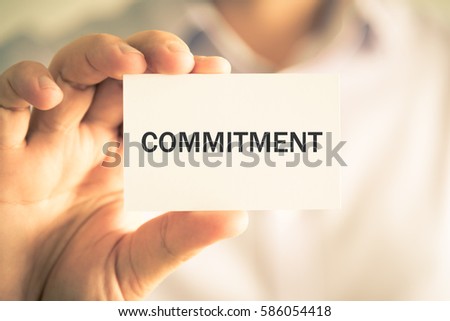 Closeup on businessman holding a card with text COMMITMENT , business concept image with soft focus background and vintage tone