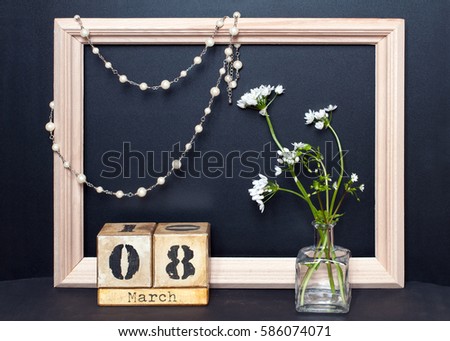 composition of flowers, beads of pearls and wood calendar for March 8 in a frame on a black background