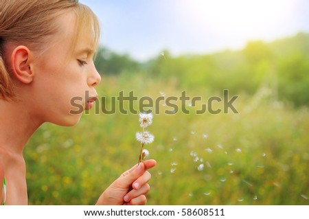 A girl blowing a dandelion flower against a background of green spring grass.