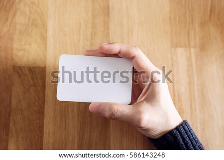 Woman holding blank business card for mock up, present over wooden desk background