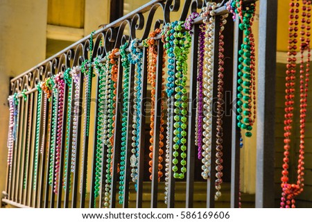 A close-up shot of a row of mardi gras beads hanging from a balcony in the French Quarter of New Orleans, There is a tiny lizard perched on the railing.