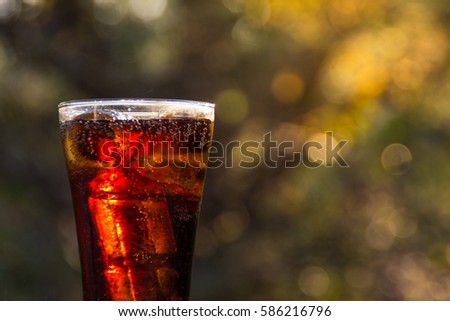 Glass of soda water with ice on the wooden table and blurred nature background