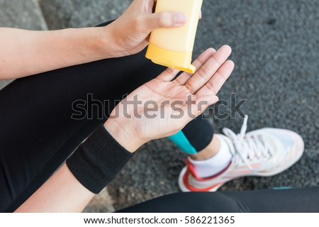 Young Asian female runner sitting down putting lotion on hand and arm ready for running exercise in the morning for healthy sport running exercise summer spring skincare sunny day concepts Royalty-Free Stock Photo #586221365