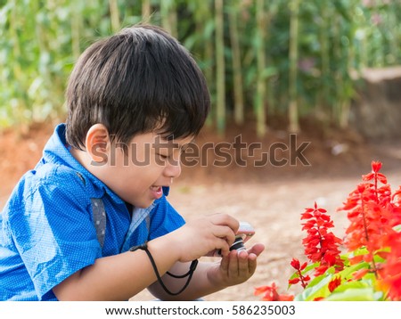Little asian boy take camera on garden flower,