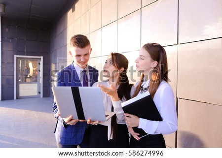 Young man and two attractive smart young women, business people, students communicate, holding laptop and study work plan, familiarize with presentation