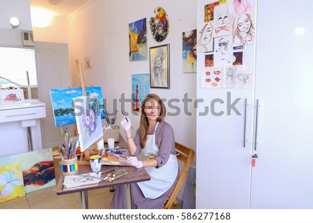 Young Woman Artist Draws Oil Painting With Purple Flowers on a White Canvas