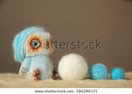 Photo of furry toy owl with a balls of wool yarn. They are dressed in warm knit hats. Photo illustration is suitable for warm clothing advertising, woolen thread.