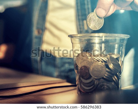 Saving money concept preset by Male hand putting money coin into the glass