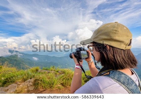 Hiker asian teens girl with backpack looking photo on digital camera is beautiful landscape natural of sierra and sky during sunset on mountain at Phu Chi Fa Forest Park, Chiang Rai, Thailand