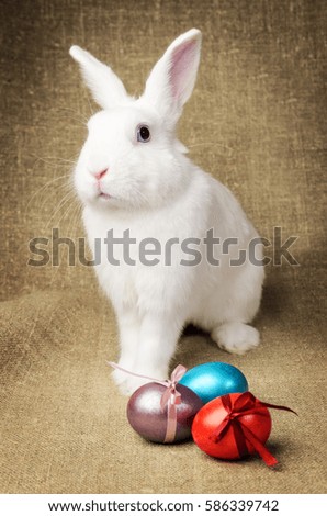 White clean beautiful Easter bunny next to a wicker basket with eggs in the background natural burlap cloth